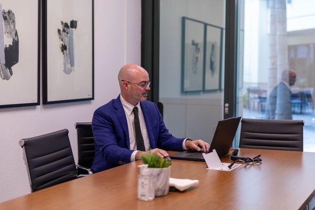 Man in a blue suit working on a laptop at a conference table in a modern office meeting room