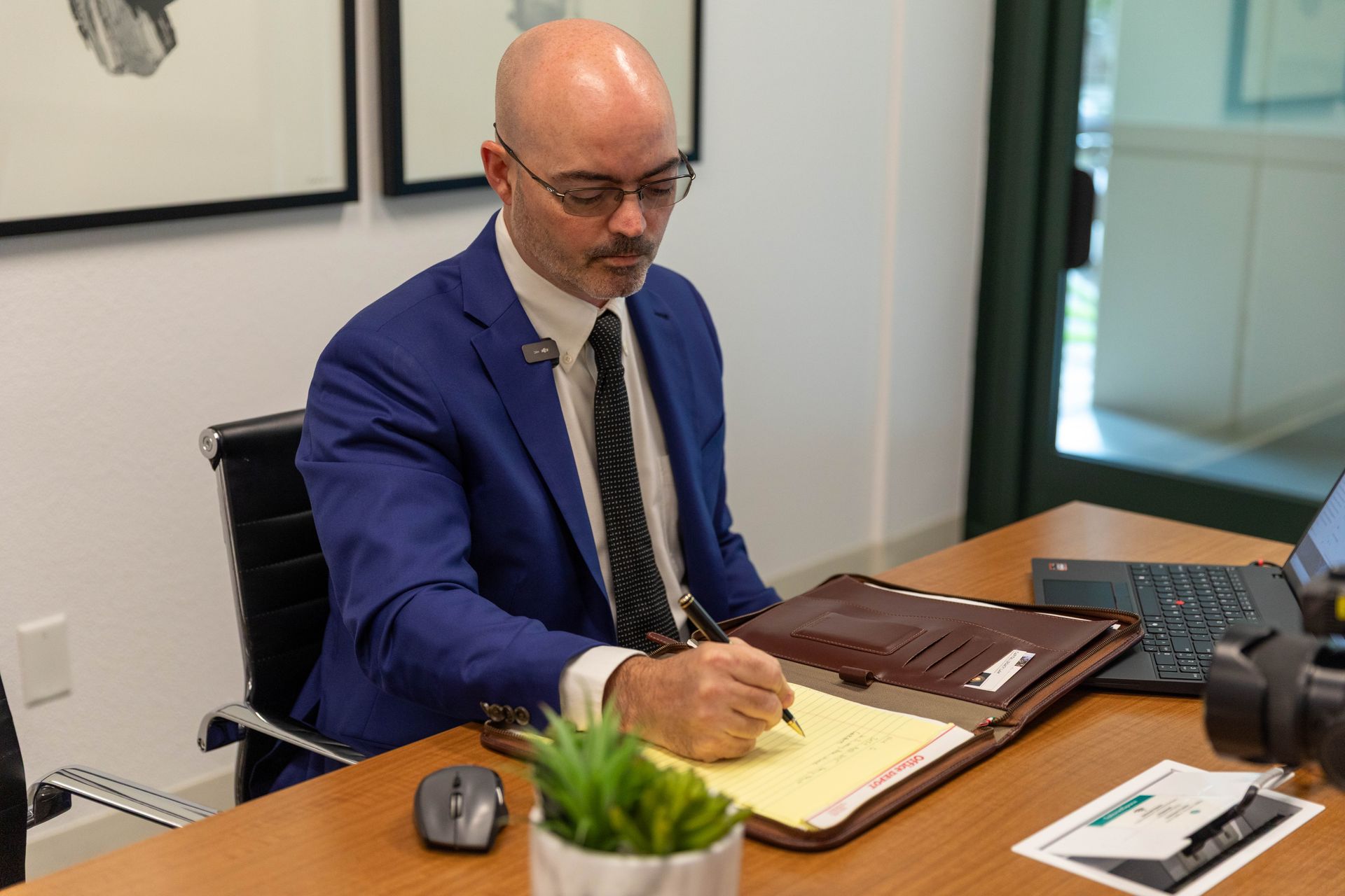 Man in a blue suit writing at a desk in an office meeting room