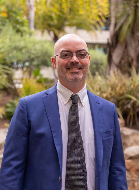 Smiling man in blue blazer and tie standing outdoors in a garden setting