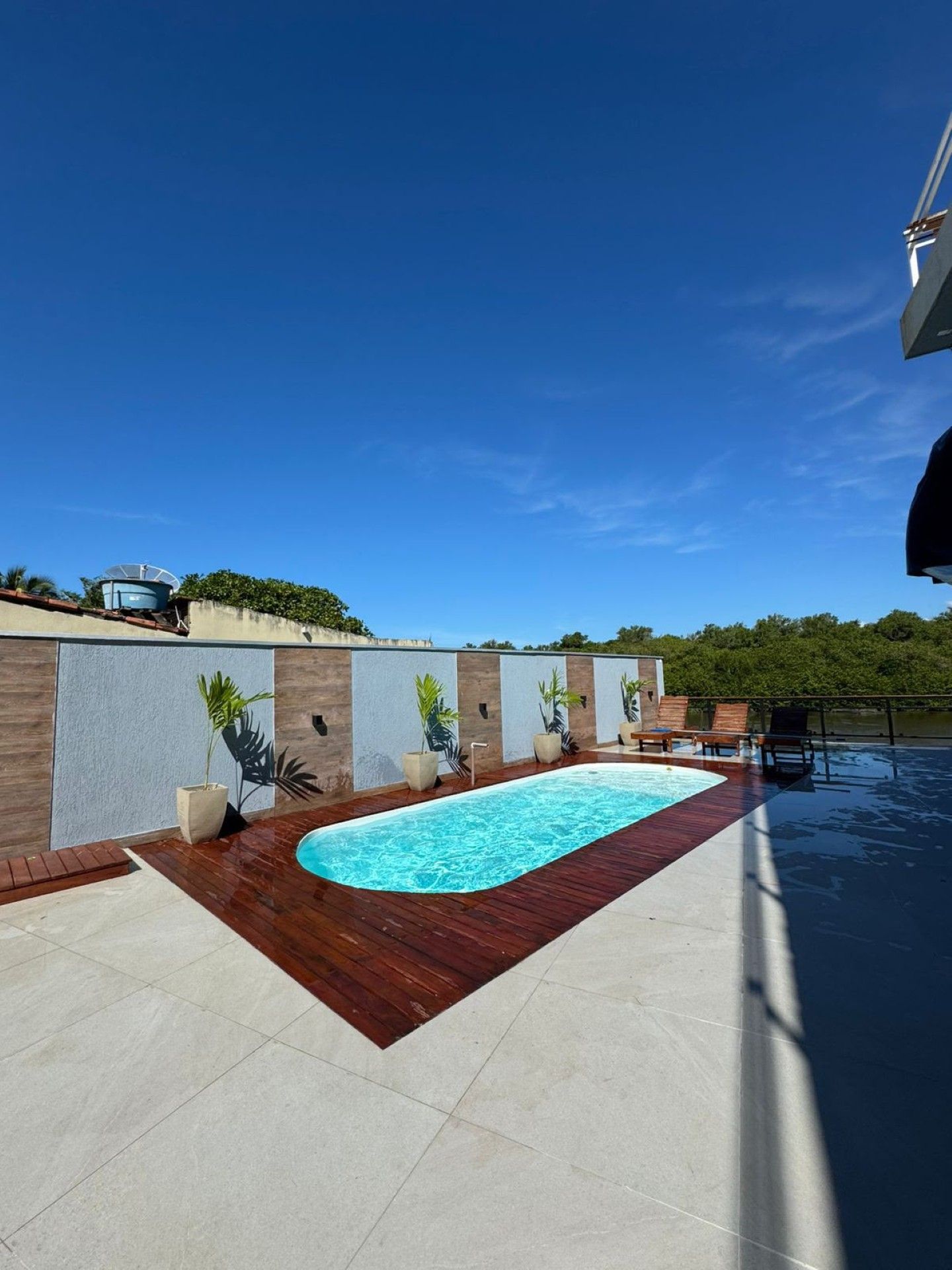 Piscina moderna no quintal, com deck branco, revestimento de madeira e céu azul límpido