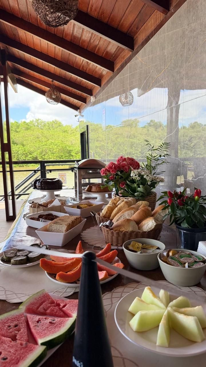 Buffet de café da manhã com diversas opções gastronômicas em um balcão de madeira, com um mural colorido ao fundo.
