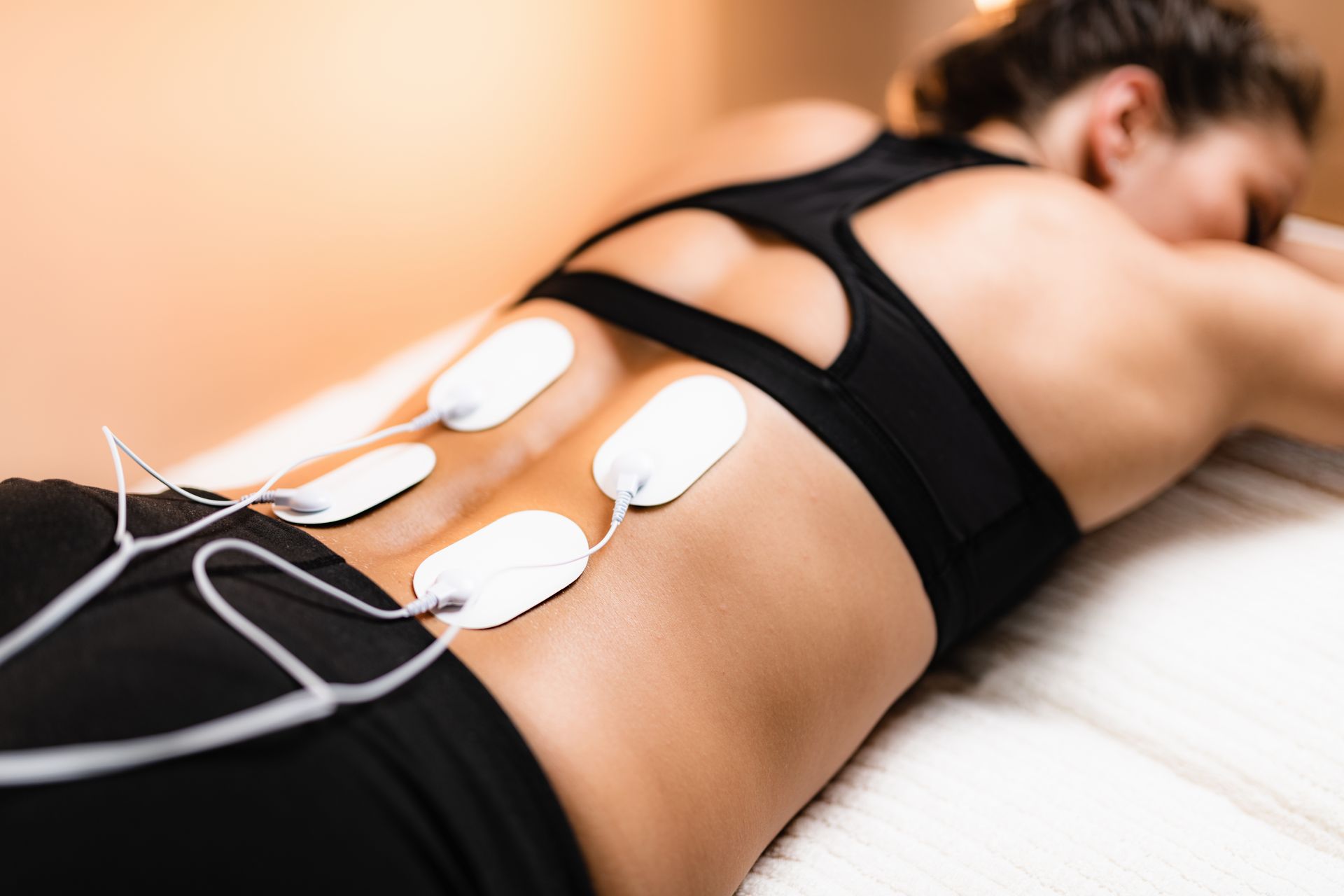 A woman is laying on a bed with electrical pads on her back.