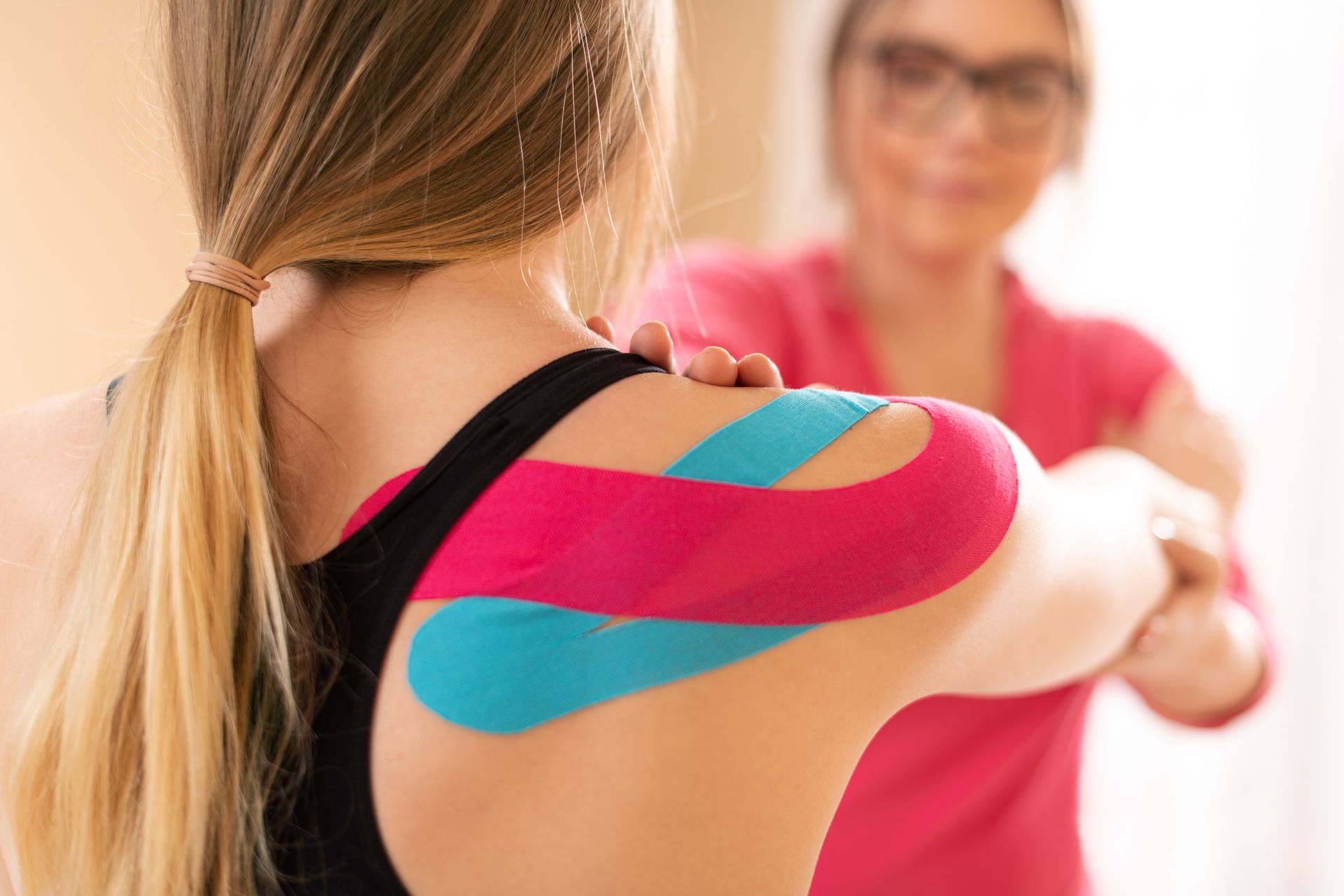 A woman with kinesio tape on her shoulder is being examined by a doctor.