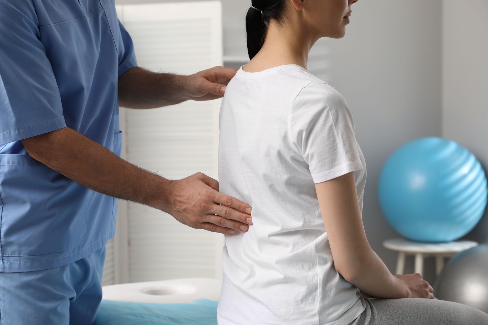 A woman is sitting on a bed while a doctor examines her back.
