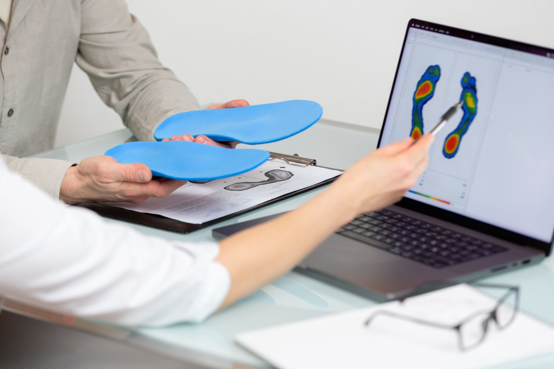 A person is holding a pair of insoles in front of a laptop computer.