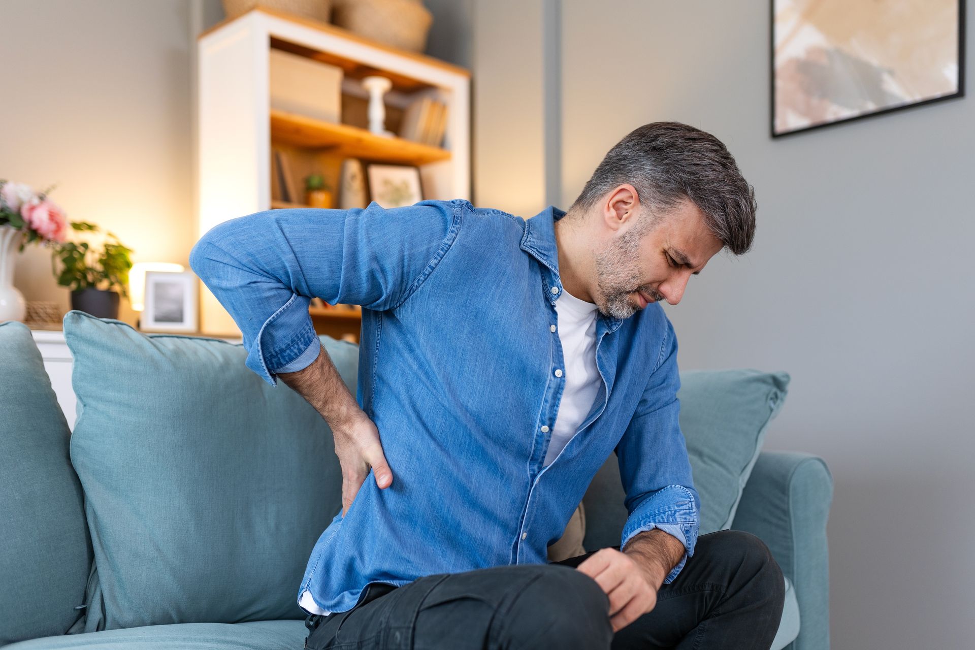 A man is sitting on a couch holding his back in pain.