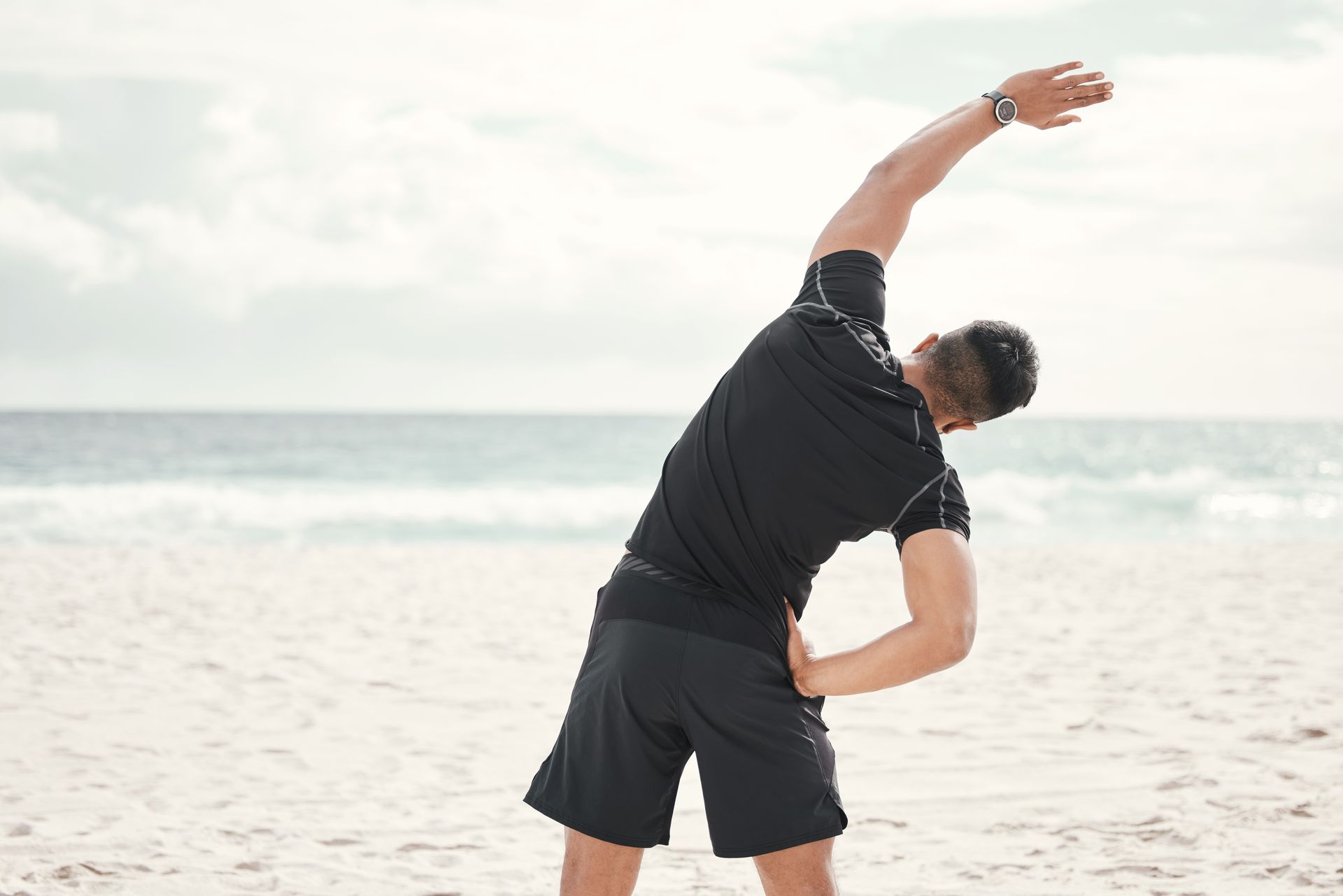 A man is stretching his arms on the beach.