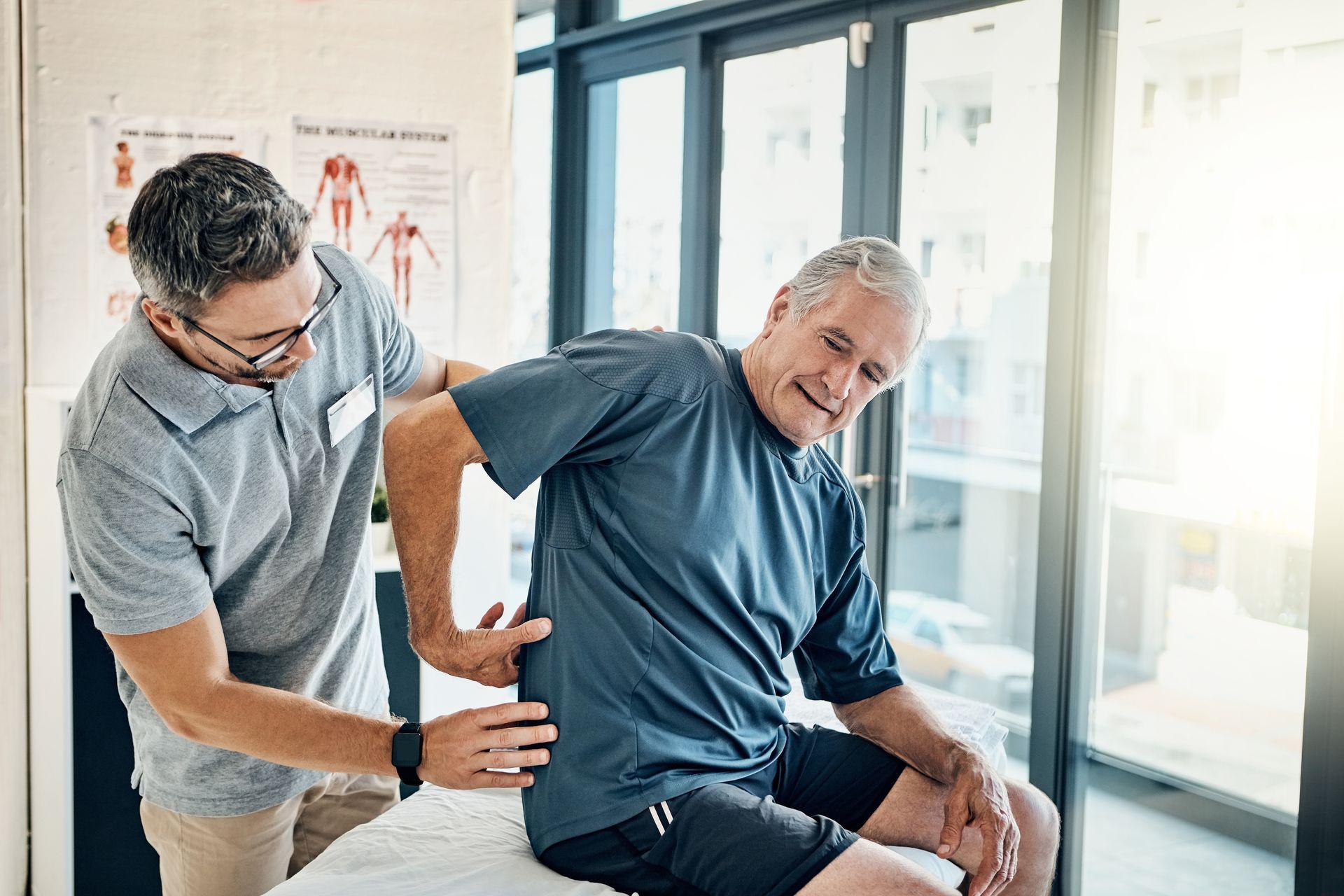 A man is sitting on a table while a doctor examines his back.
