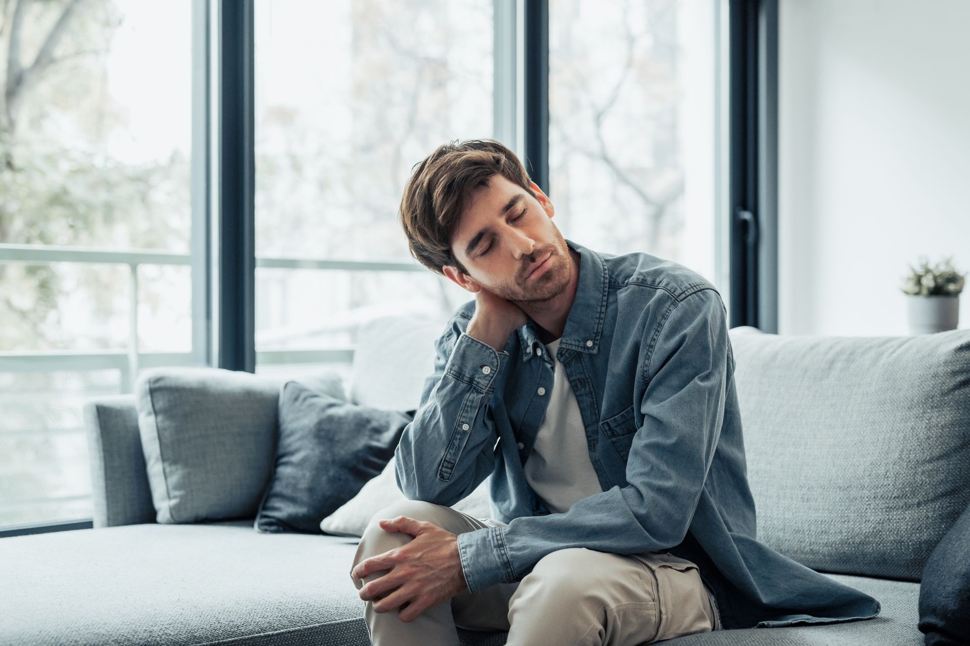 A man is sitting on a couch with his head resting on his hand.