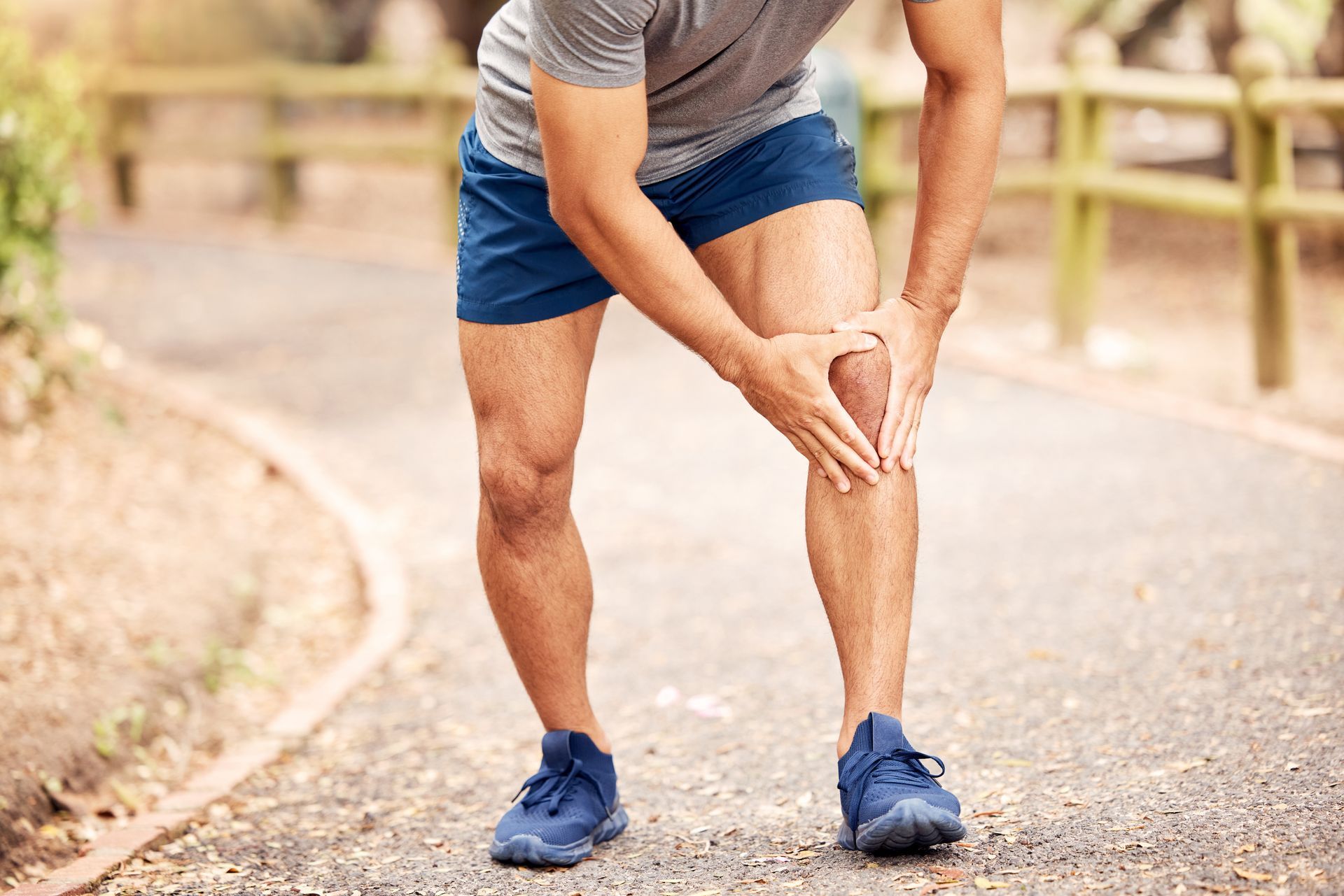 A man is holding his knee in pain while standing on a path.