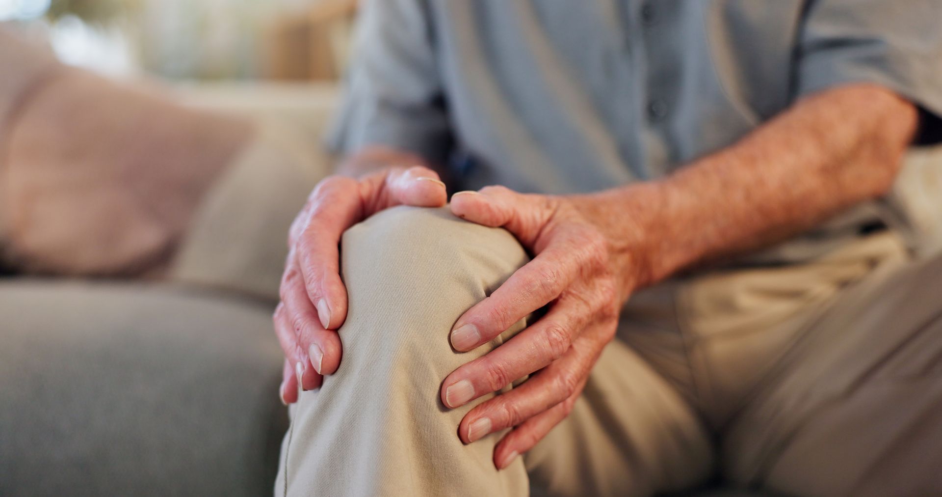 A man is sitting on a couch holding his knee in pain.