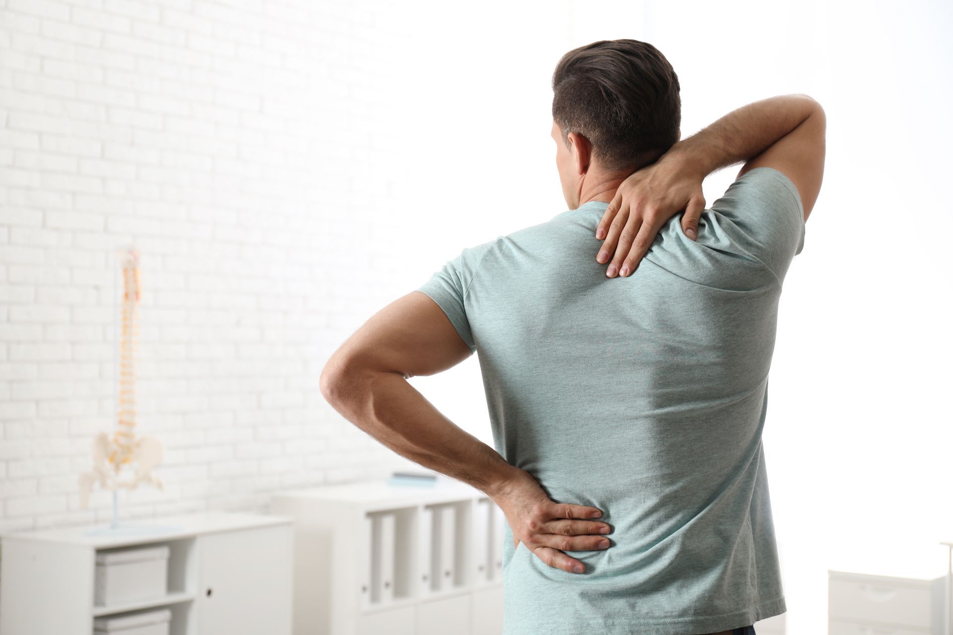 A man is holding his back in pain while standing in a room.