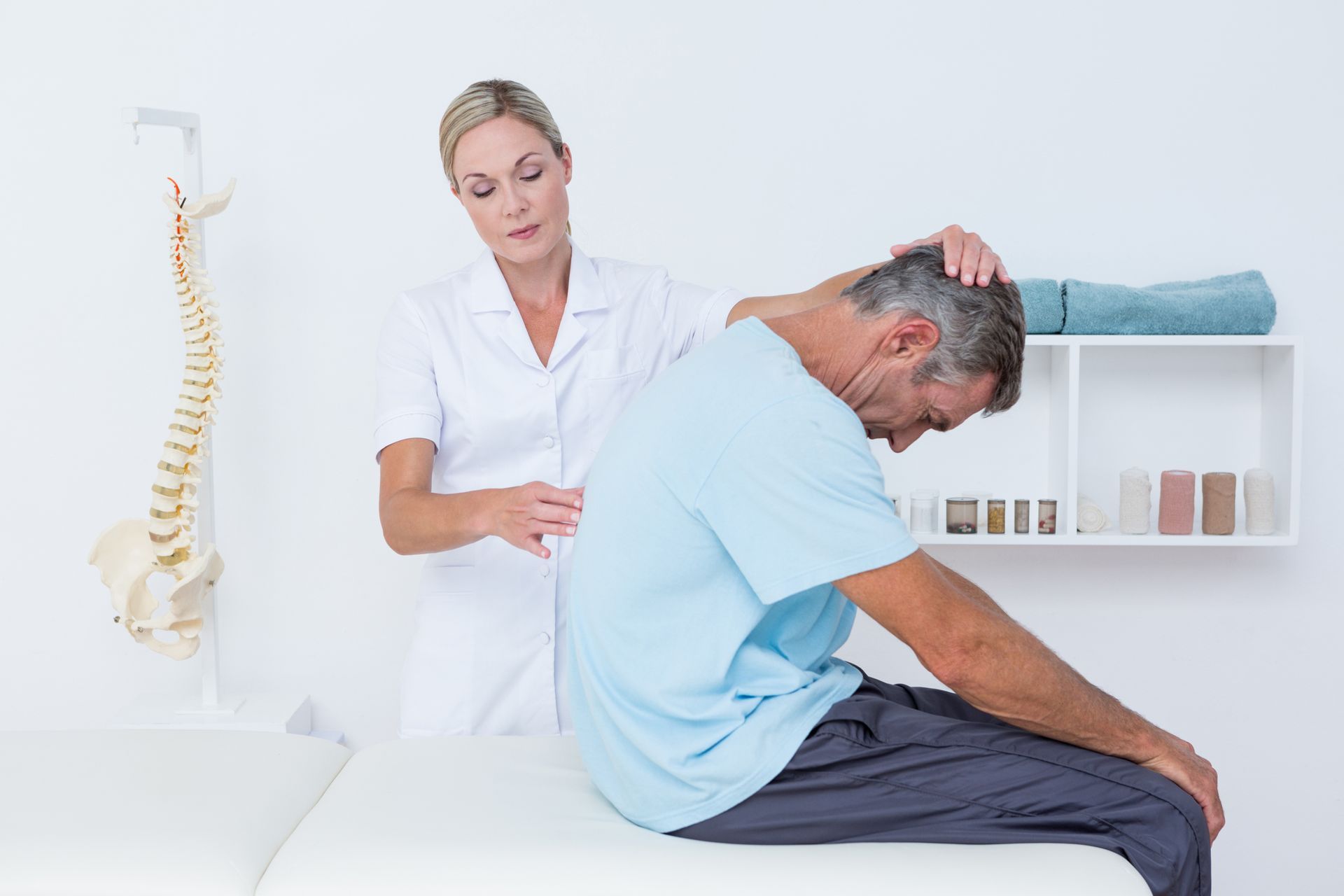 A man is sitting on a bed while a nurse examines his back.