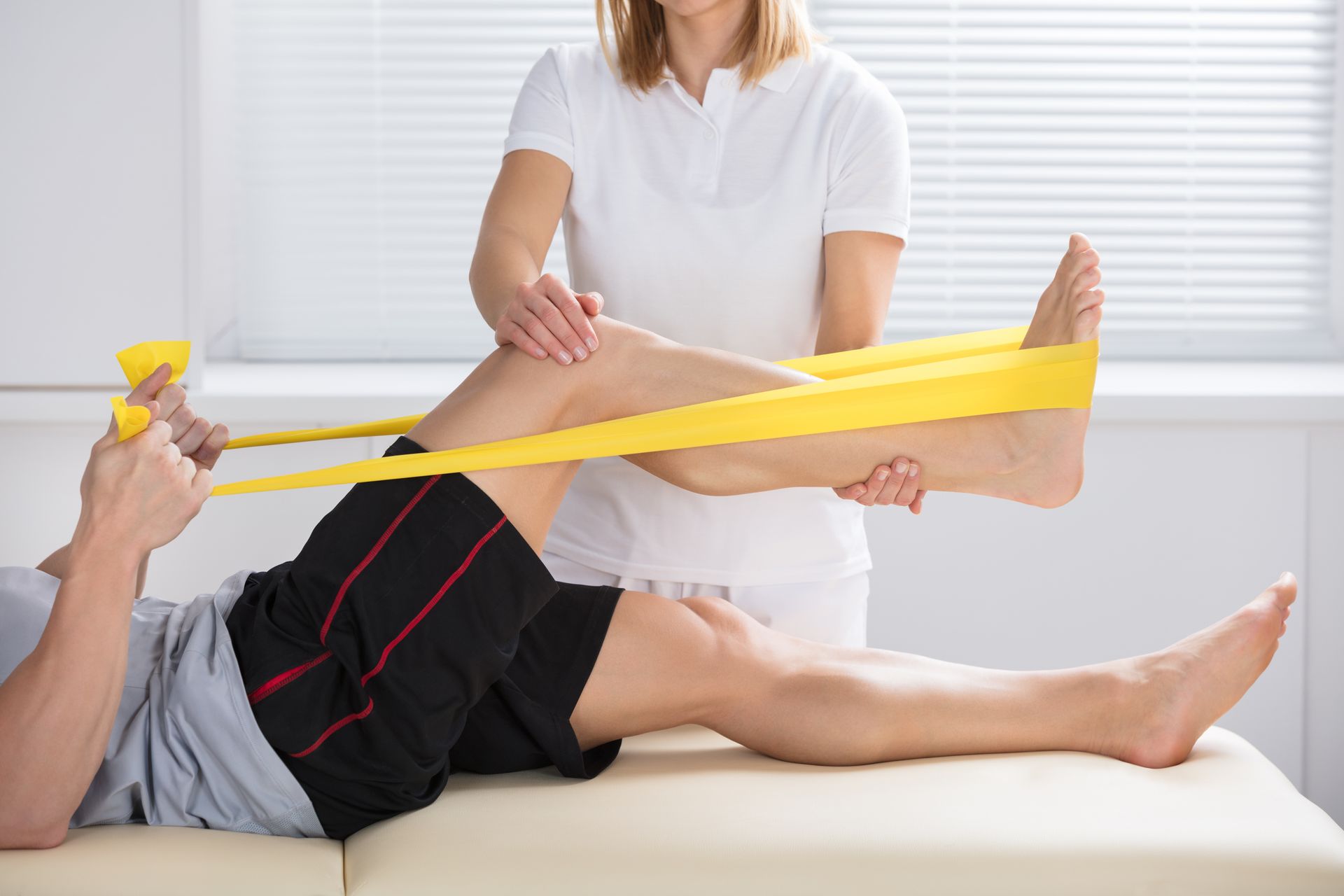 A woman is helping a man with a resistance band on his leg.