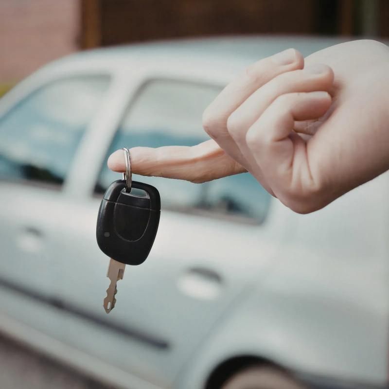 A hand holding a car key fob in front of a white car.