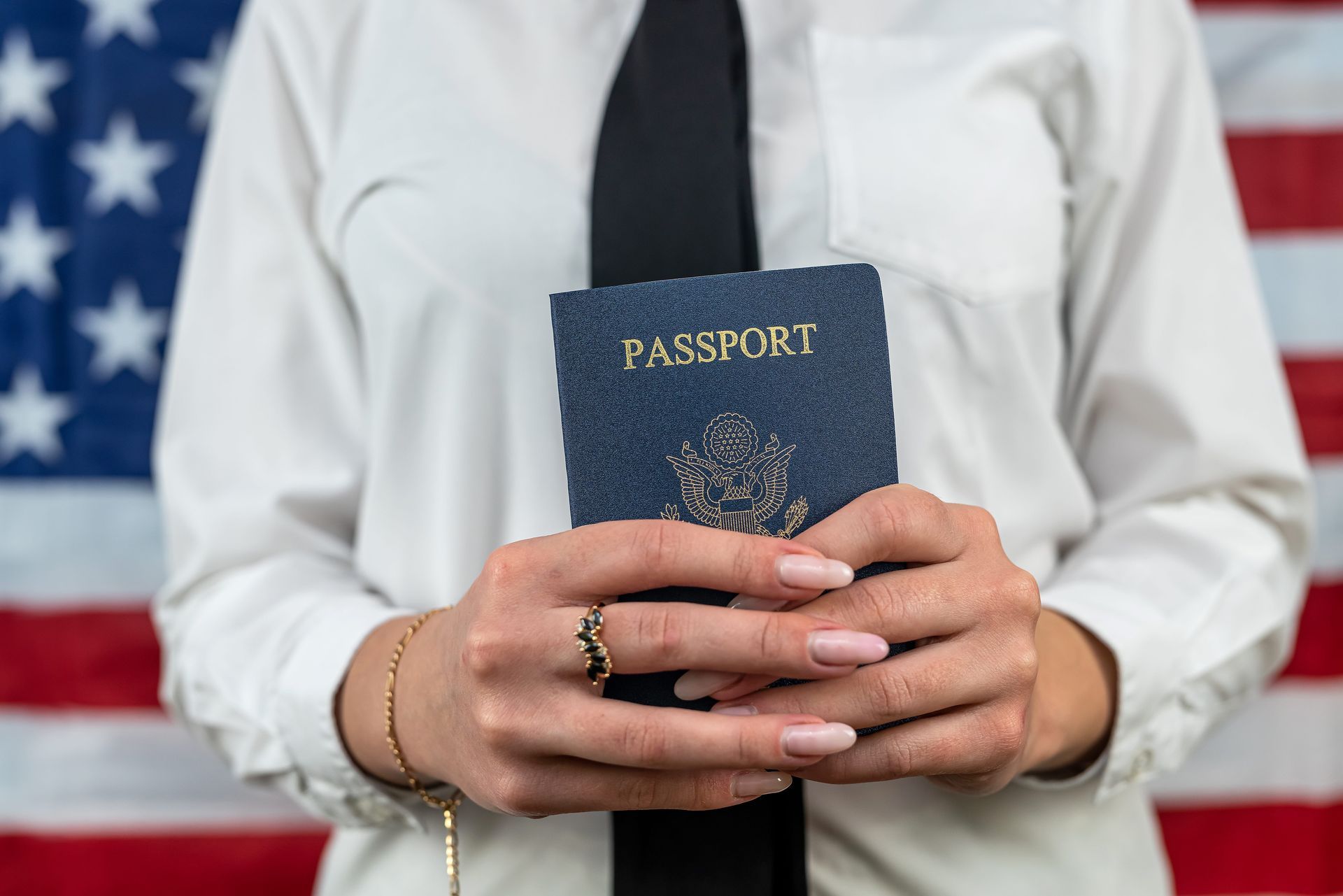 Person holding a blue passport in front of a U.S. flag backdrop