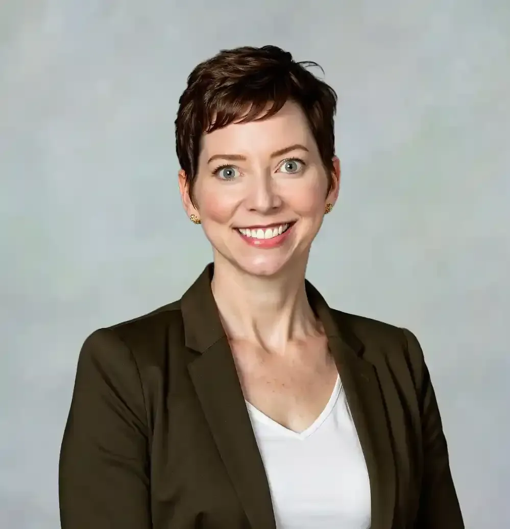 A woman wearing a black jacket and pearls is smiling for the camera.