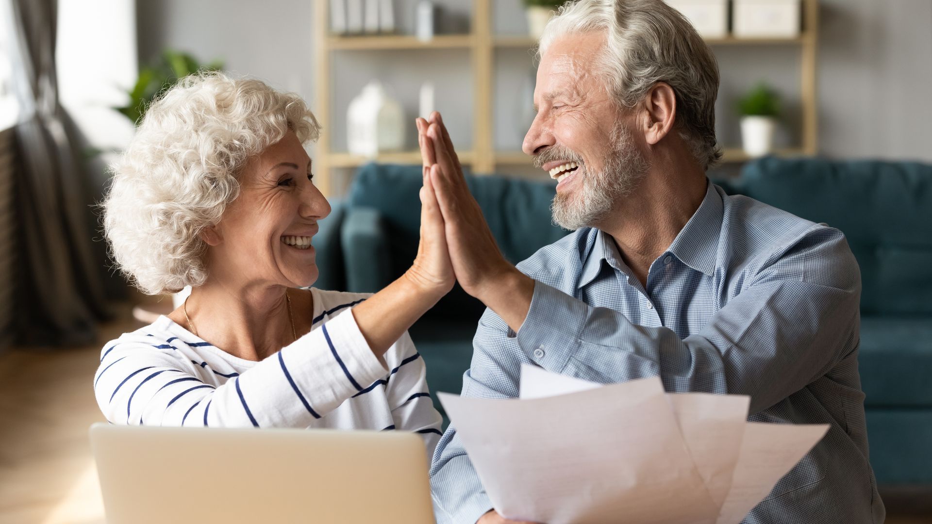 Two smiling people high-five at a table with papers in a bright office.