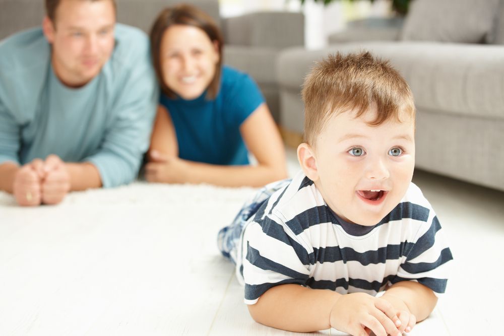 Smiling child lying on a bed with two adults blurred in the background