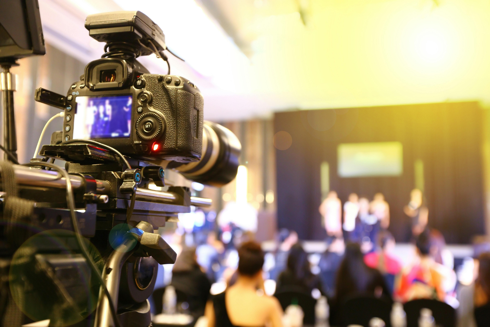 Camera filming a blurred stage event with audience in the foreground