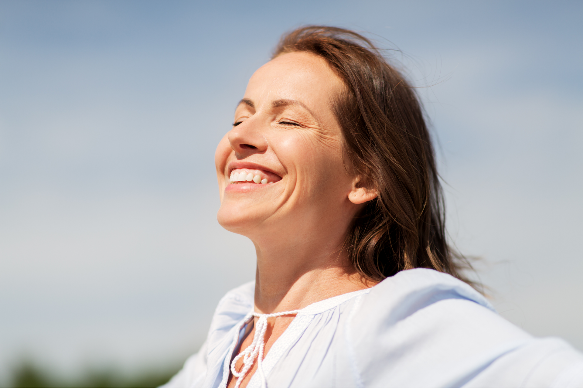 Smiling person in a white top outdoors under a blue sky