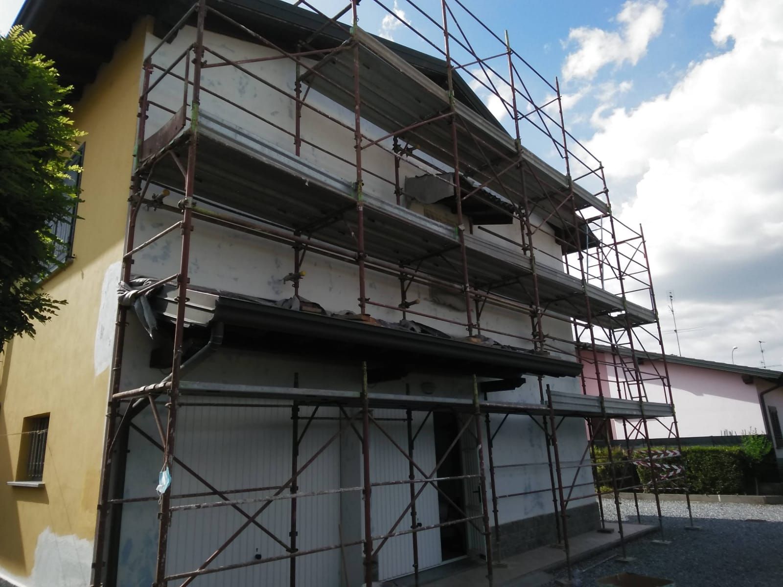 Un edificio a due piani in costruzione, ricoperto da impalcature metalliche, con pareti gialle a sinistra e bianche sul davanti.