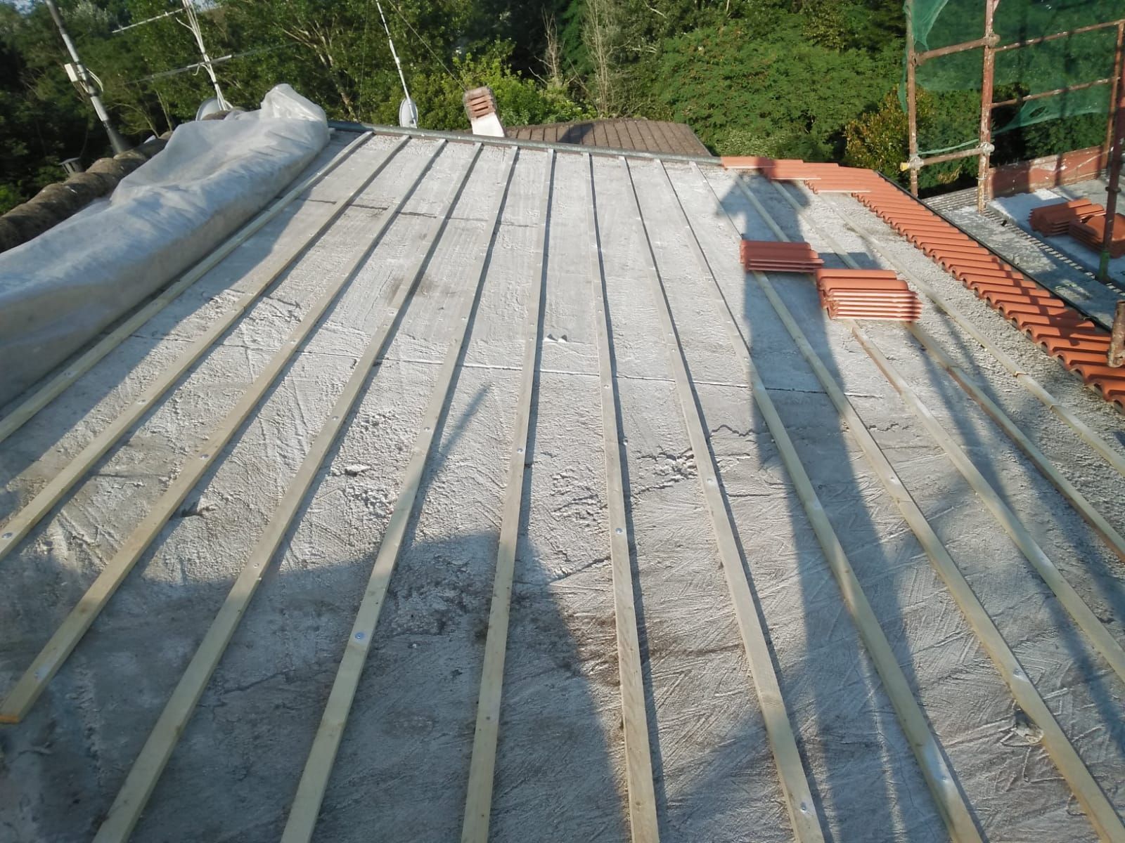 Un tetto residenziale in costruzione con listelli di legno installati su una membrana grigia, con alcune tegole rosse parzialmente posate.