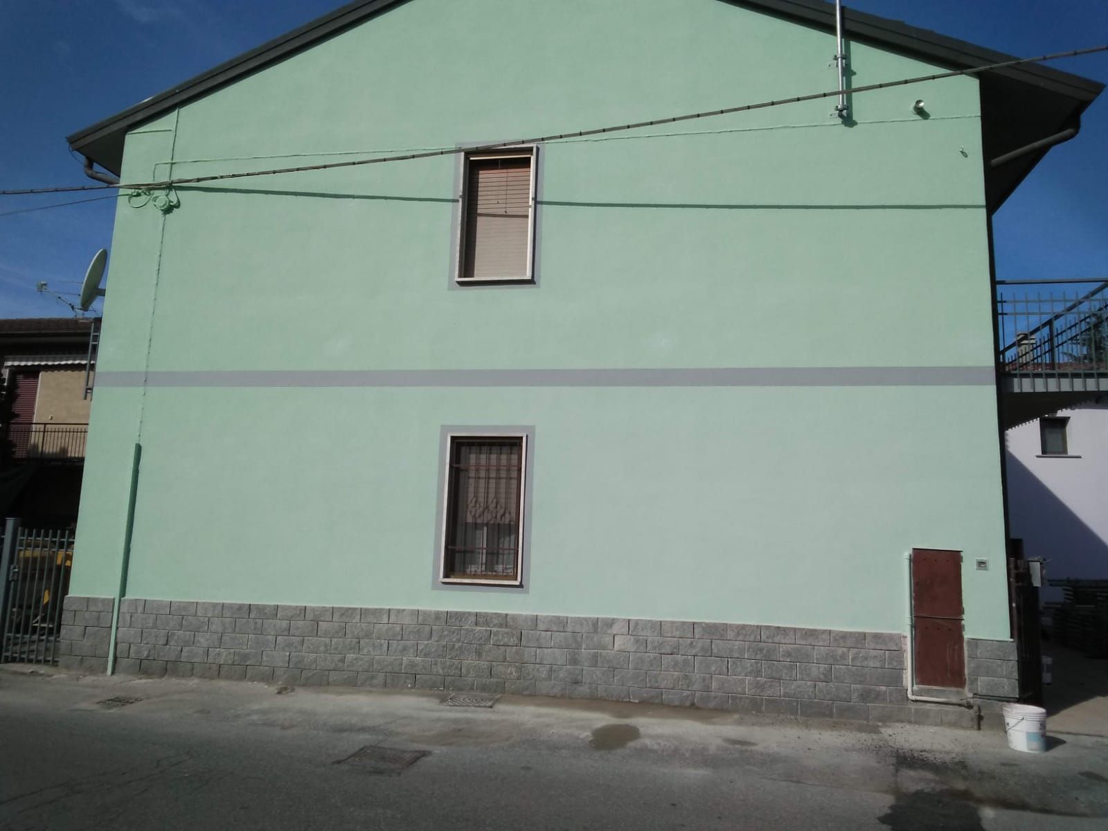 Una casa a due piani, di colore verde chiaro, con una base in pietra, due finestre centrali e una piccola porta scura sul lato destro.