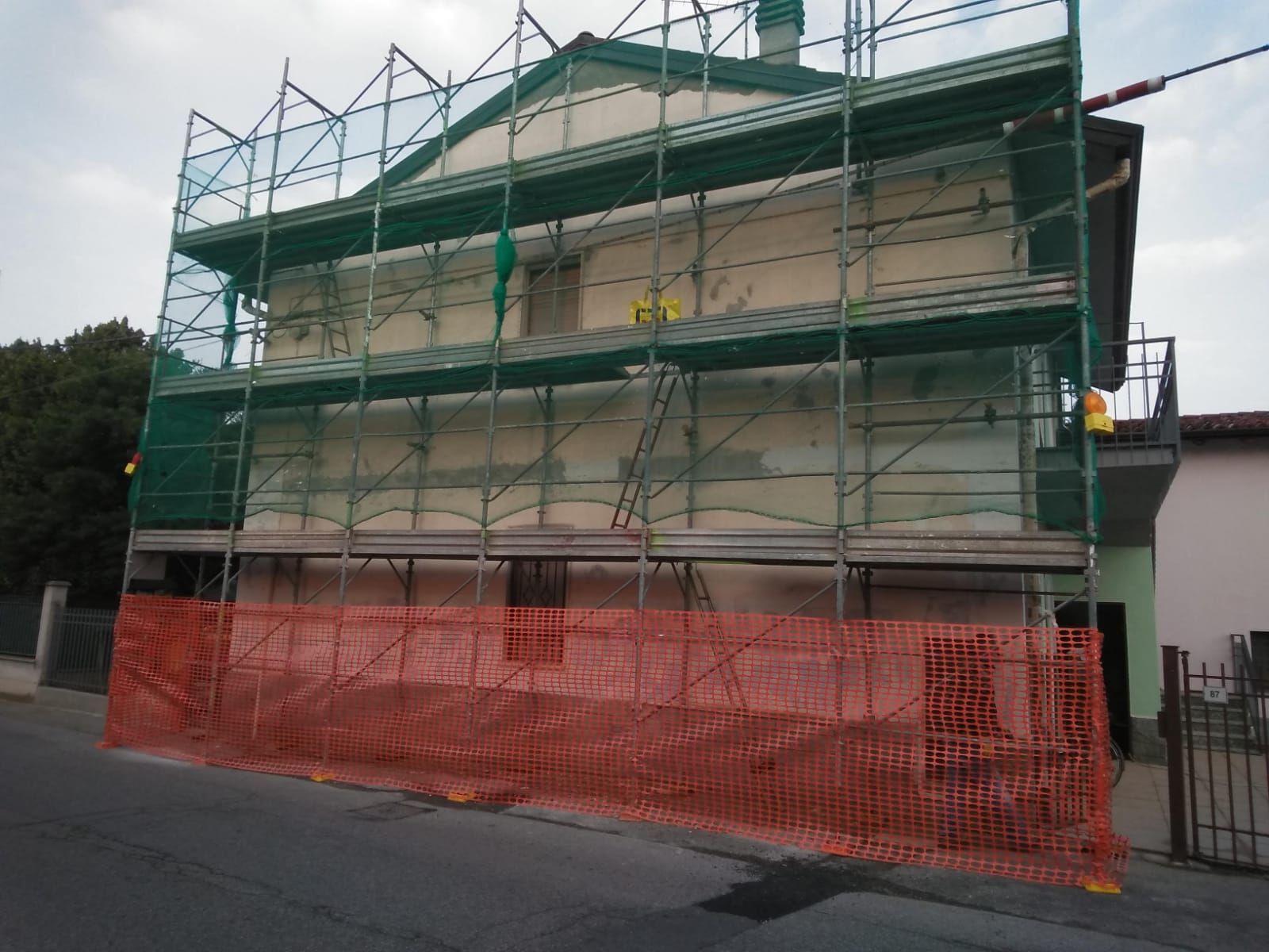 Un edificio a più piani in costruzione, circondato da impalcature metalliche verdi e protetto da una recinzione di sicurezza arancione.