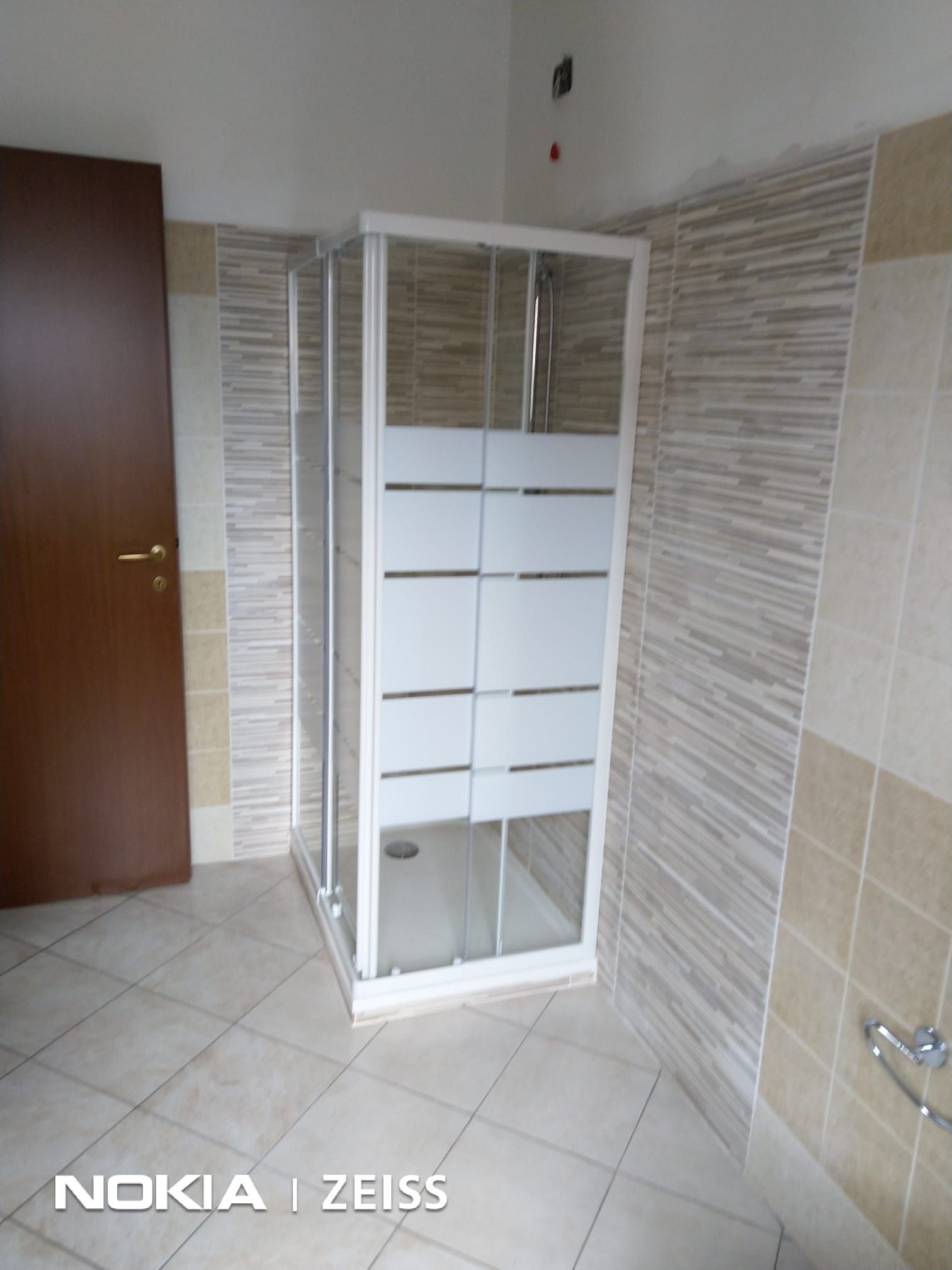 Box doccia quadrato con inserti in vetro satinato in un bagno con pareti rivestite di piastrelle beige e pavimento in piastrelle di colore chiaro.