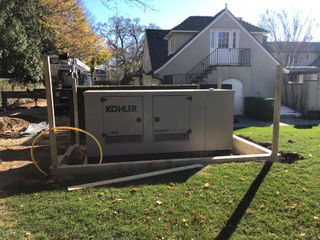 Outdoor generator beside a house, with yellow hose and fall leaves in the yard.