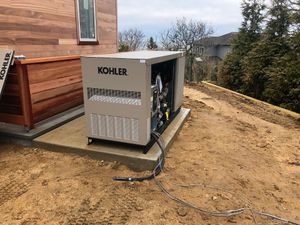 Kohler generator on a dirt slope beside a house, with cables running across the ground