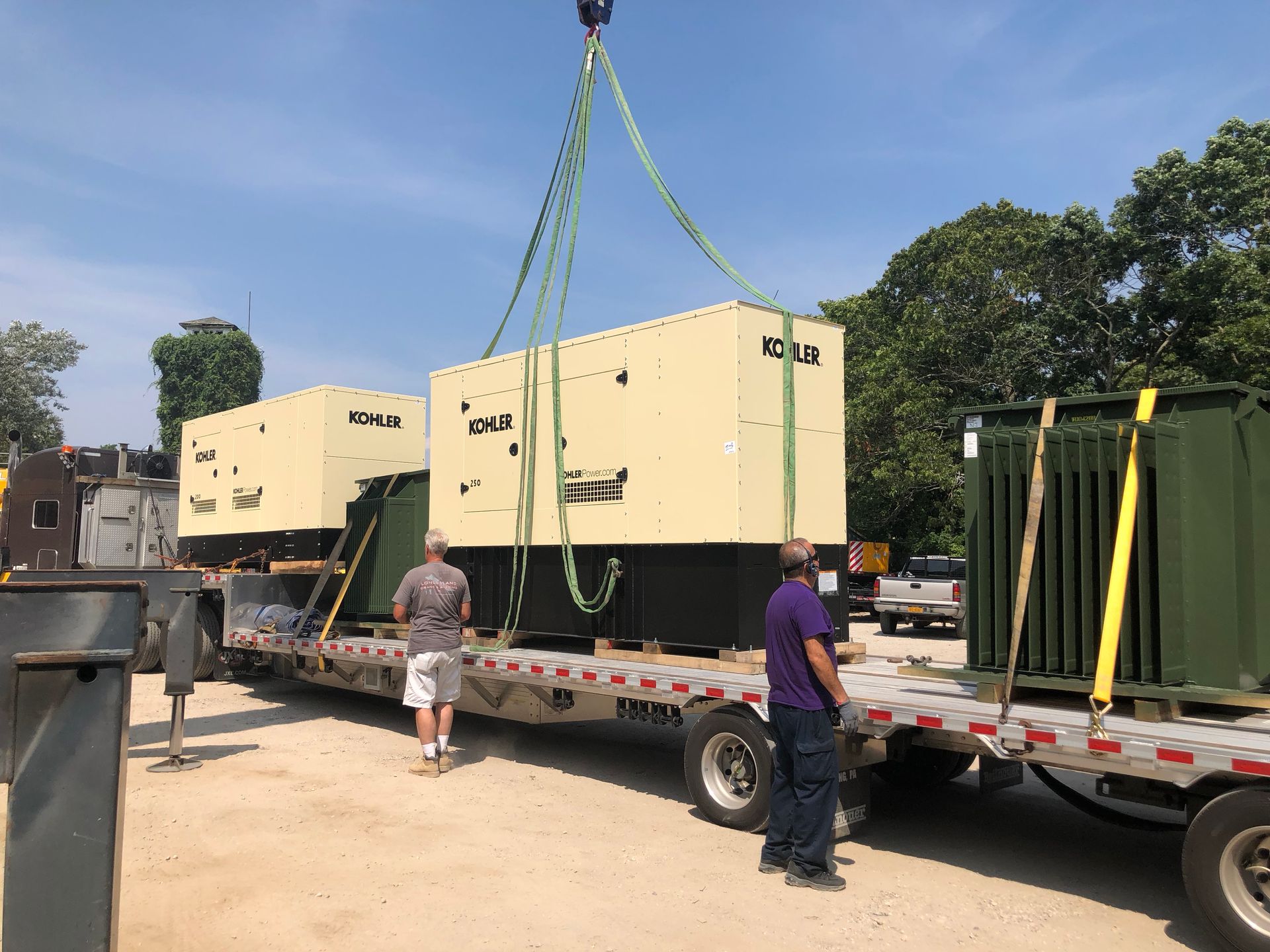 Large beige industrial machine being lifted by crane onto a flatbed trailer outdoors