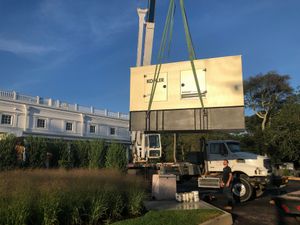 Crane lifting a large yellow prefab unit near a white building on a sunny worksite