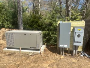 Outdoor electrical equipment and generator units beside a wooded area, including a gray box and utility panels.