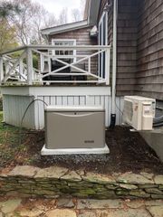Outdoor HVAC unit beneath a wooden deck beside a house, with a beige cover and white railing above.