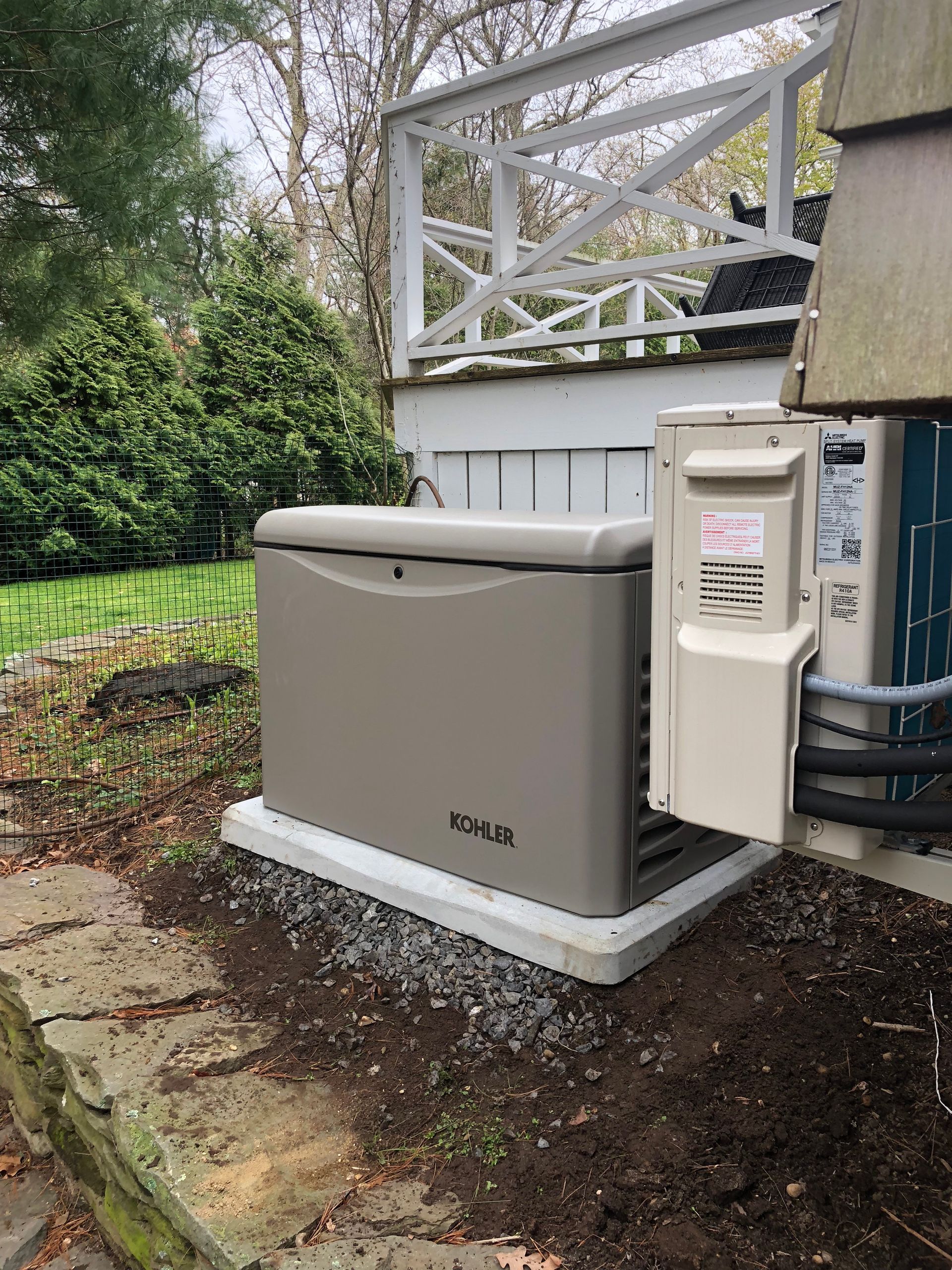 Outdoor standby generator beside a house, with white utility equipment and stone edging around it