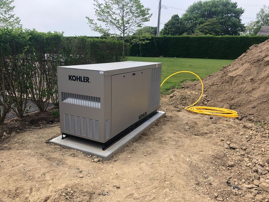 Kohler generator on a concrete pad beside a dirt mound in a landscaped yard