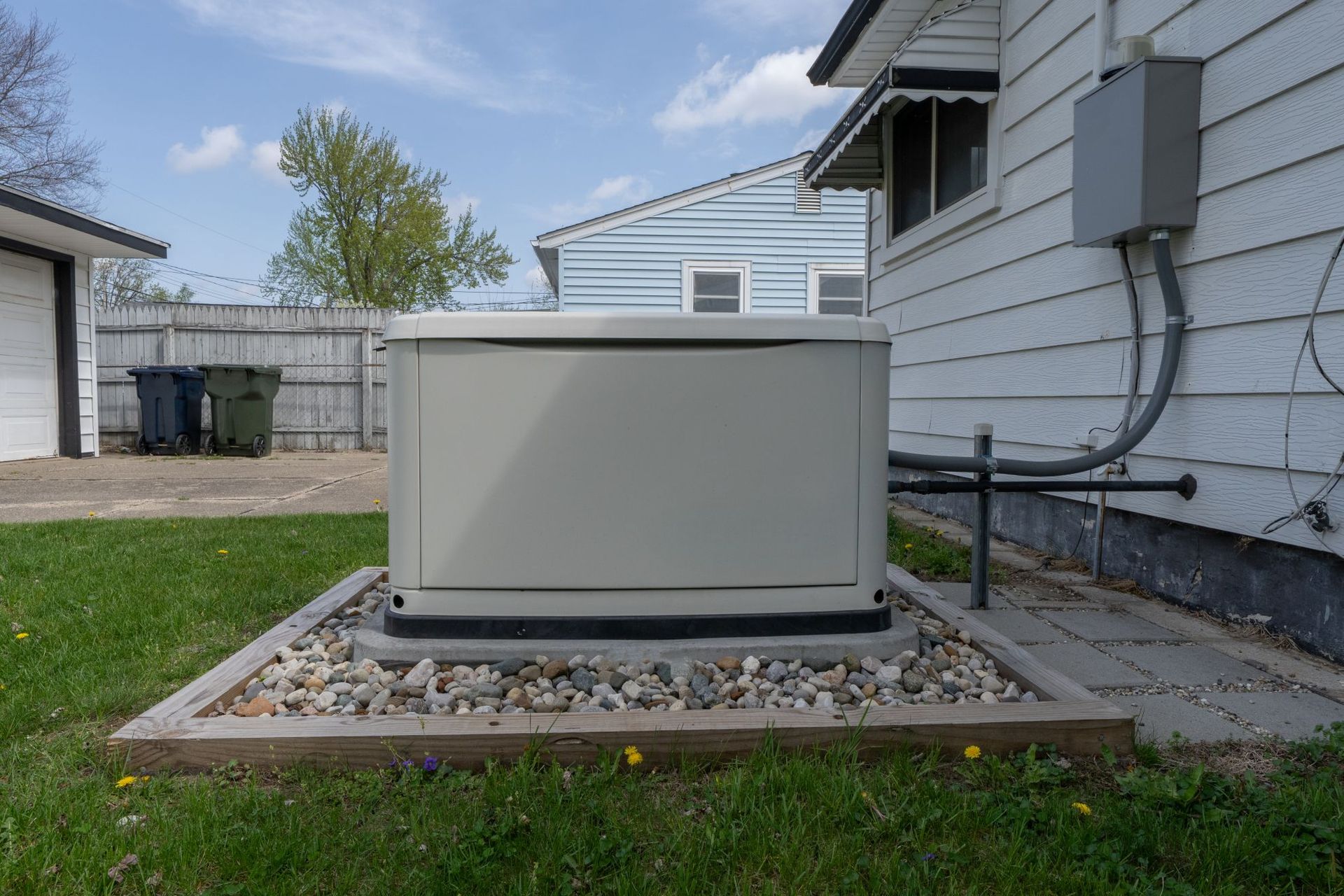 Outdoor HVAC unit beside a house on a gravel pad, with grass and a driveway nearby