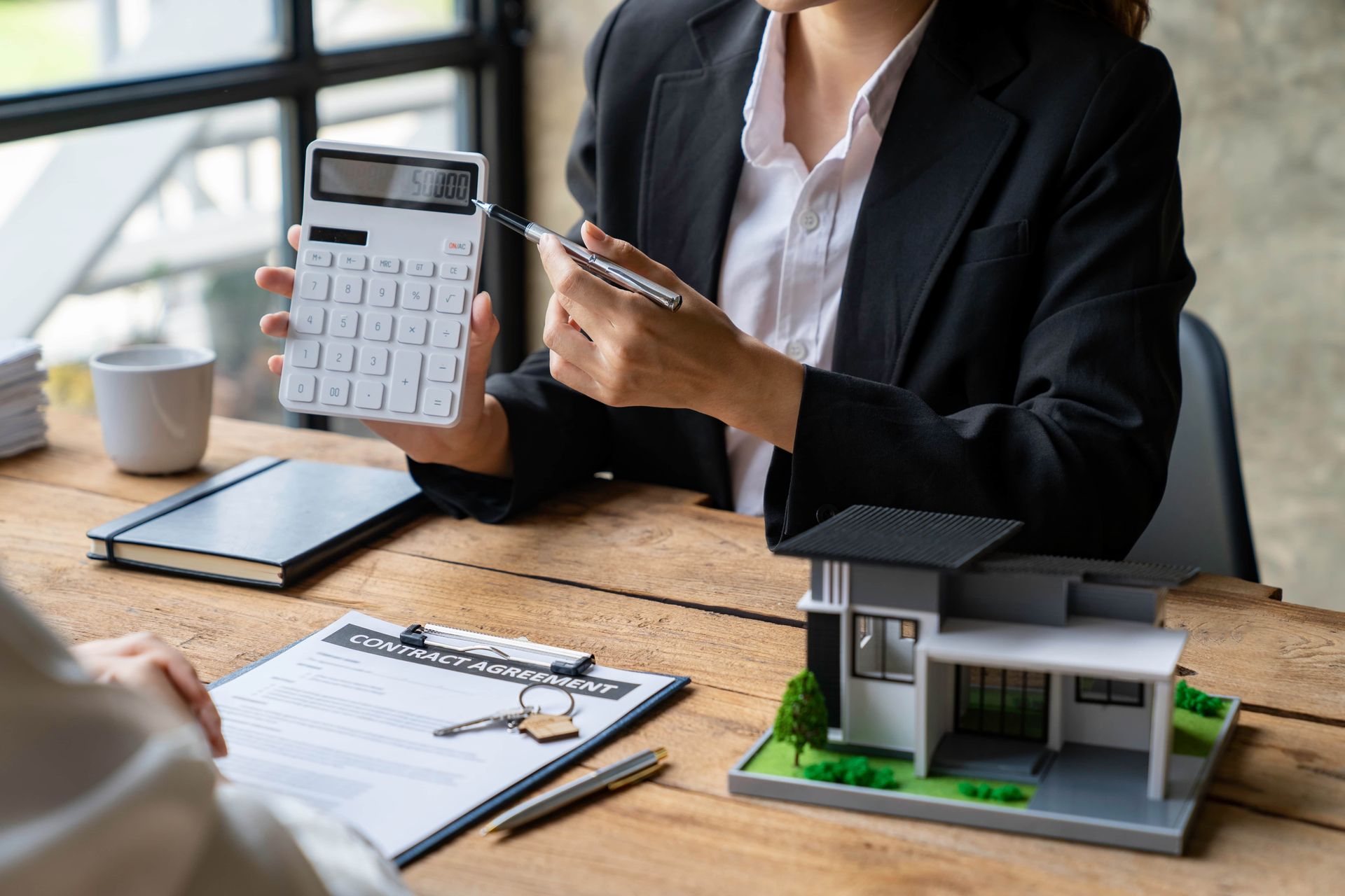 A woman is sitting at a table holding a calculator and a pen.