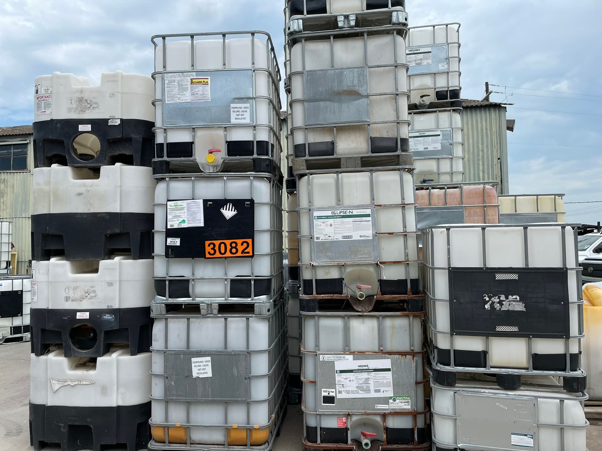 Stacked white and black plastic containers in metal cages outdoors, against a cloudy sky.