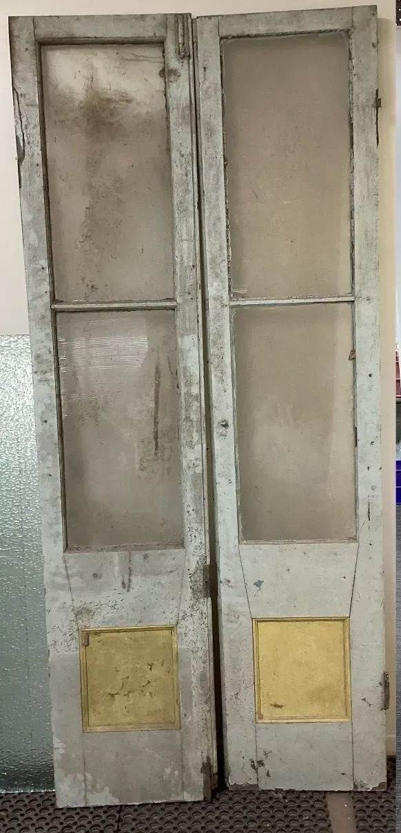 A pair of old wooden doors with glass panels are sitting next to each other.