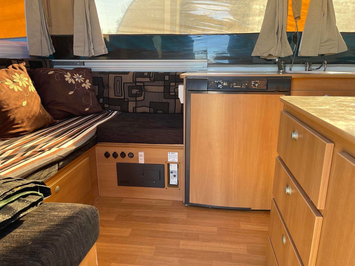 Small Camper Kitchen With Wood Cabinets, Compact Fridge and Bench Seating — B & C Caravan Service Pty Ltd In Dubbo, NSW