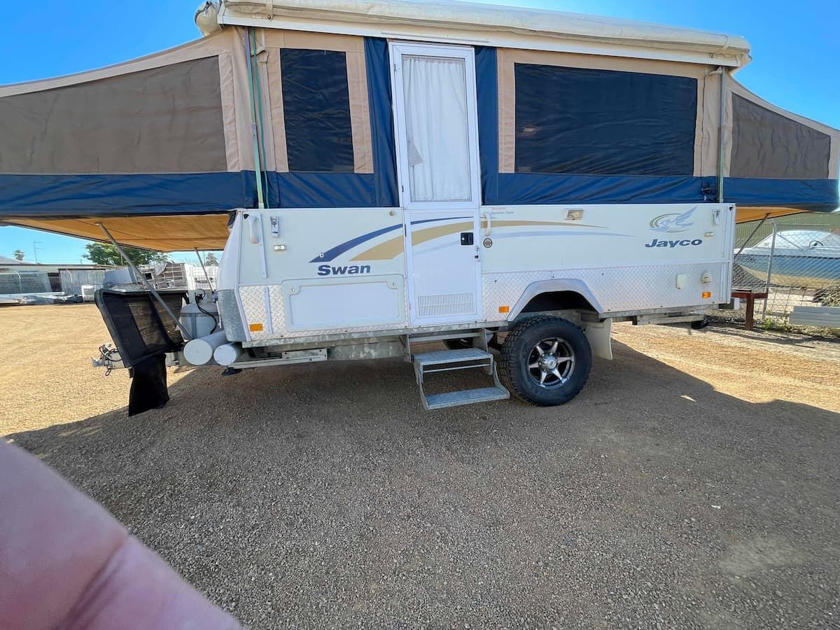 White Camper Trailer With Blue Awnings Parked on Gravel — B & C Caravan Service Pty Ltd In Dubbo, NSW