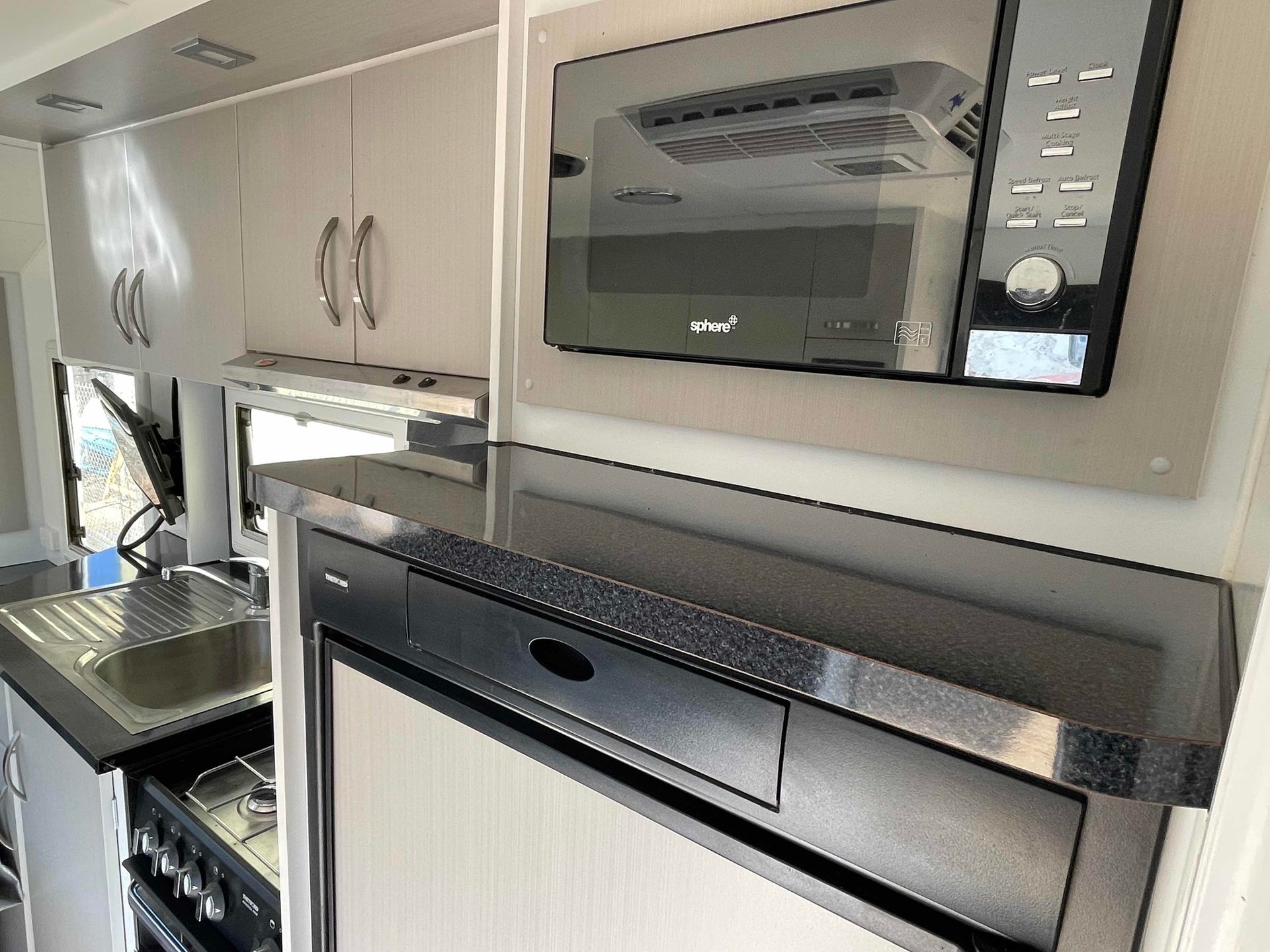 Compact Kitchen with White Cabinets, Black Countertop, and Built In Microwave and Oven Units — B & C Caravan Service Pty Ltd In Dubbo, NSW