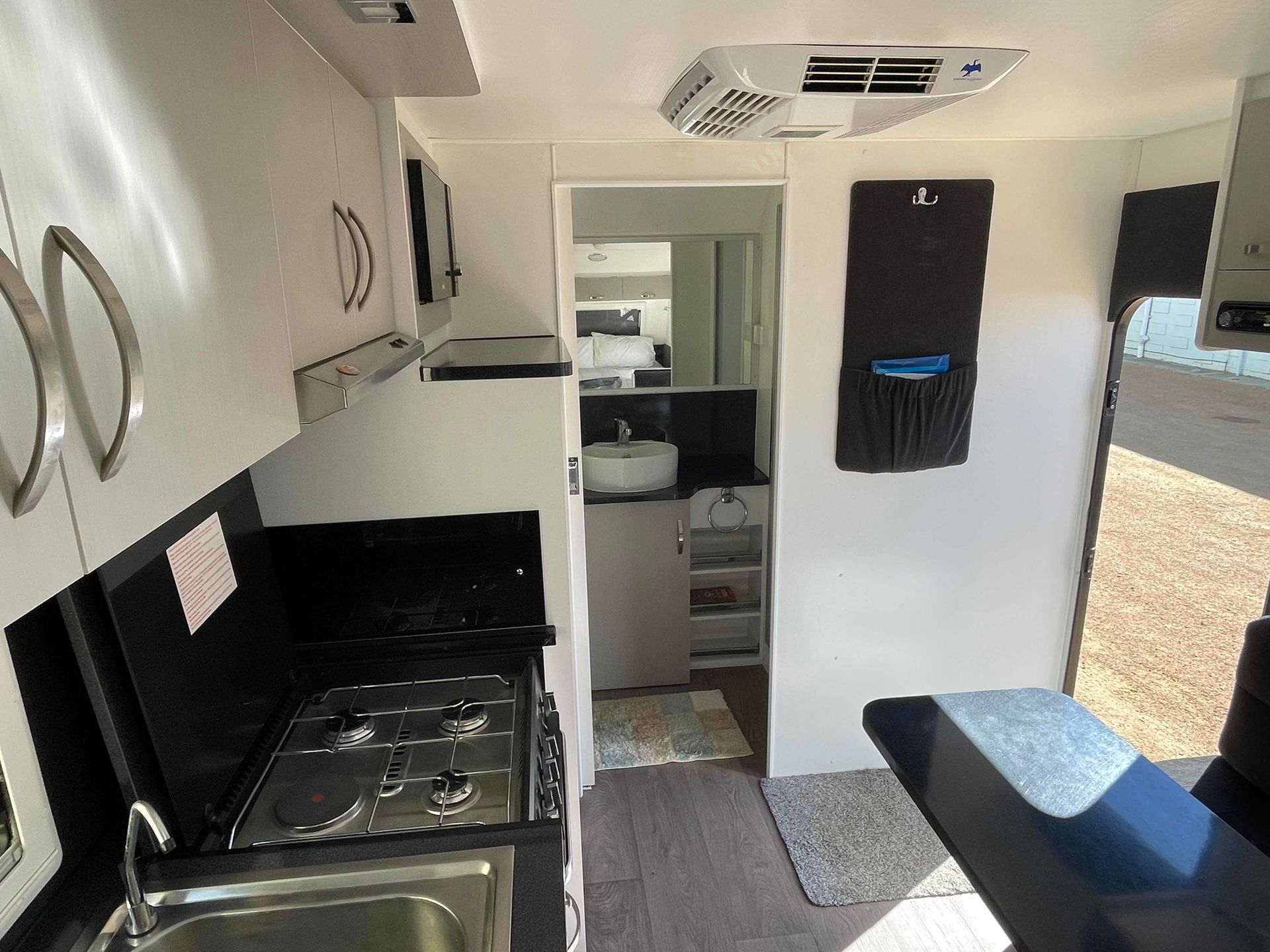 Compact RV Kitchen and Living Area with White Cabinets, Black Countertops, and Bunk Beds in The Back — B & C Caravan Service Pty Ltd In Dubbo, NSW