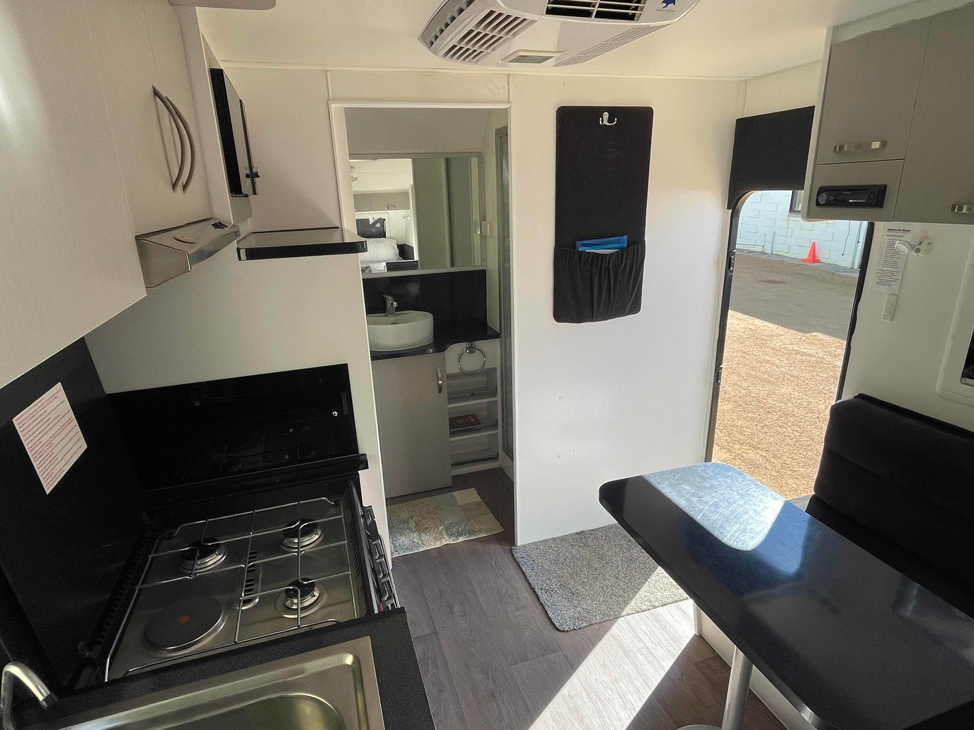 Compact Camper Kitchen with Black Counter, Sink, Stove, Bench Seat, and A View of The Outdoors — B & C Caravan Service Pty Ltd In Dubbo, NSW