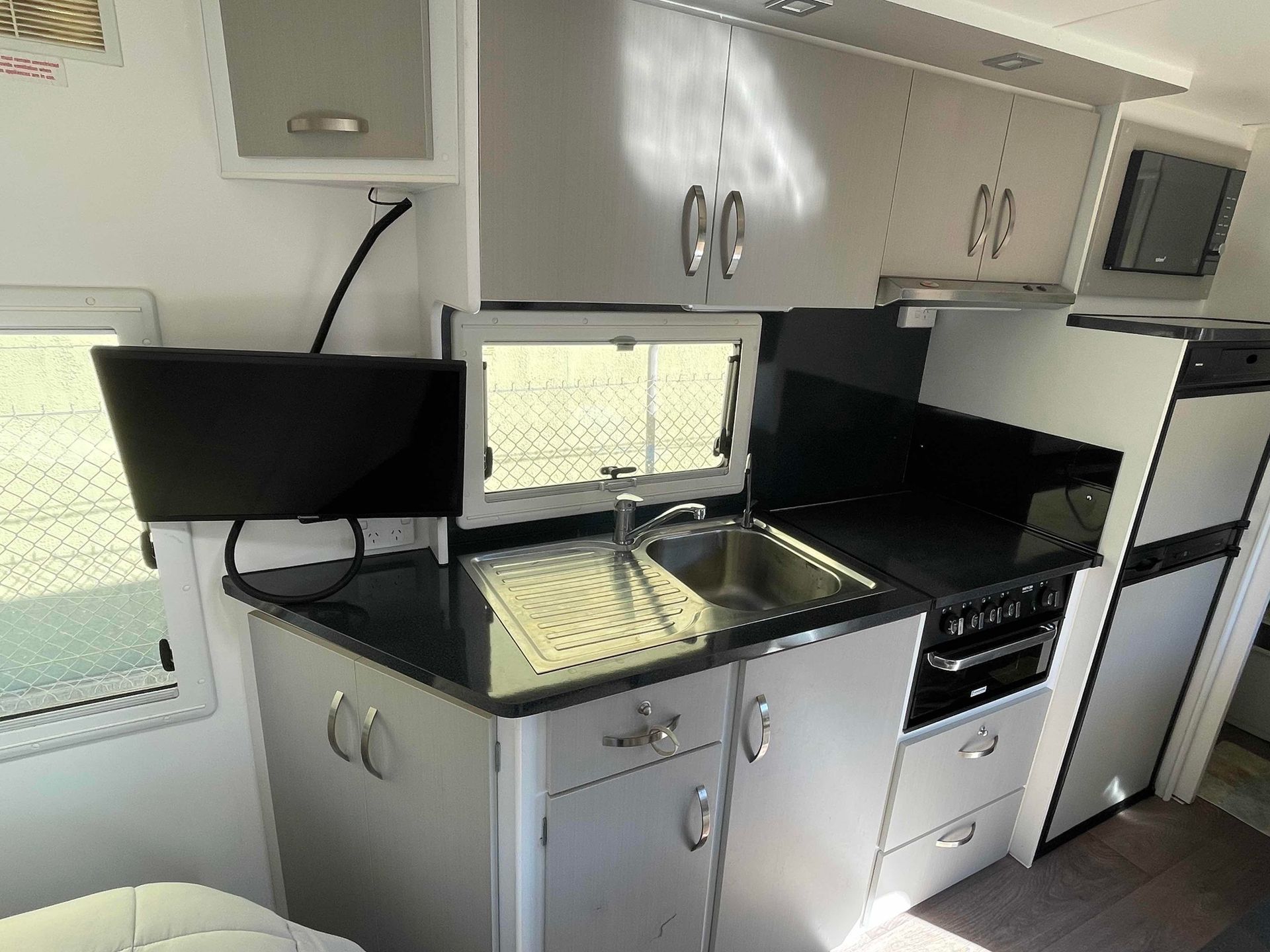 Compact Modern Kitchenette with Black Countertops, Sink, Cabinets, Fridge, and Microwave in A Bright Room — B & C Caravan Service Pty Ltd In Dubbo, NSW