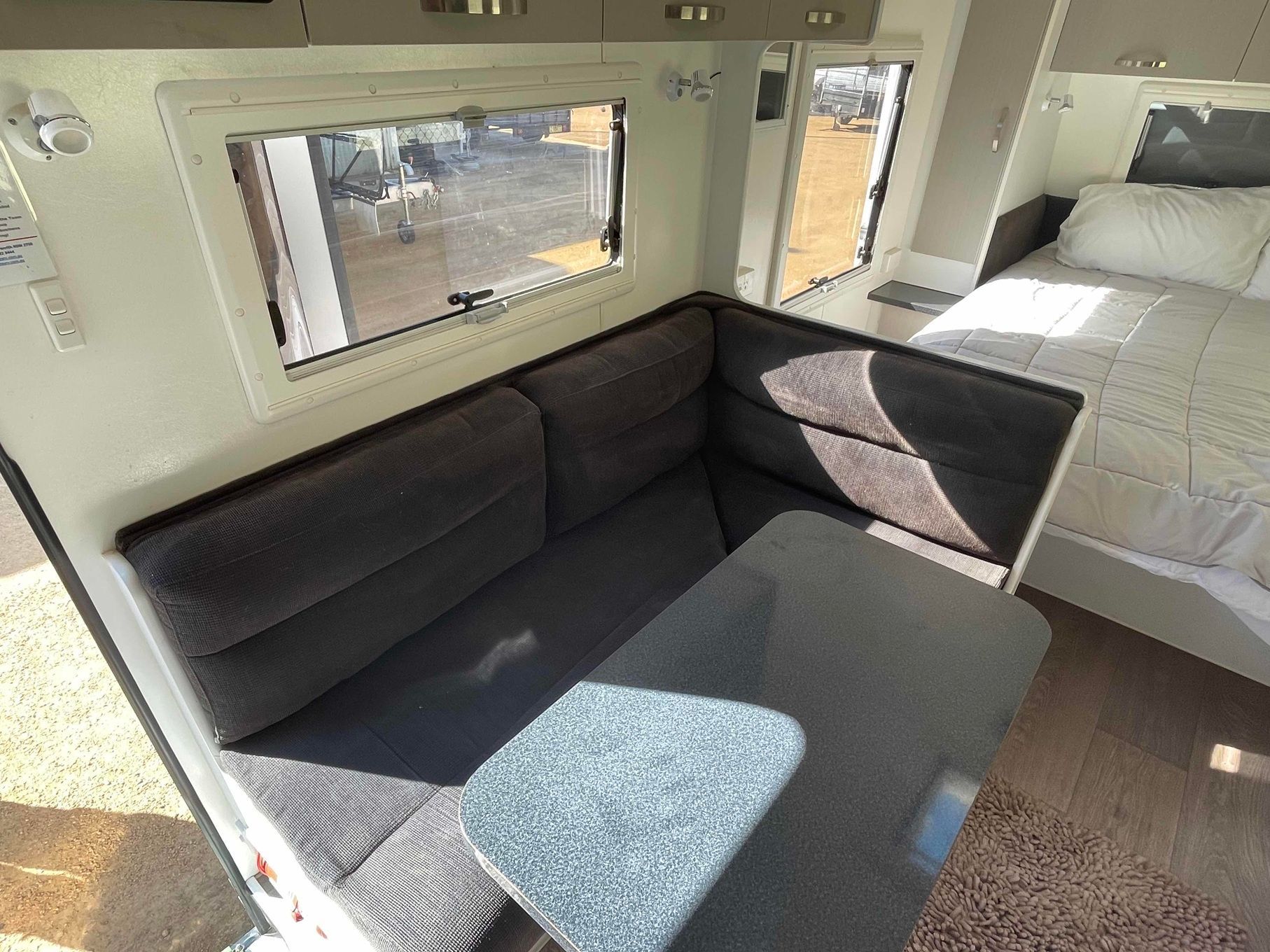 Compact Rv Lounge with Dark Sofa, Gray Table, and Bed by Sunlit Windows — B & C Caravan Service Pty Ltd In Dubbo, NSW