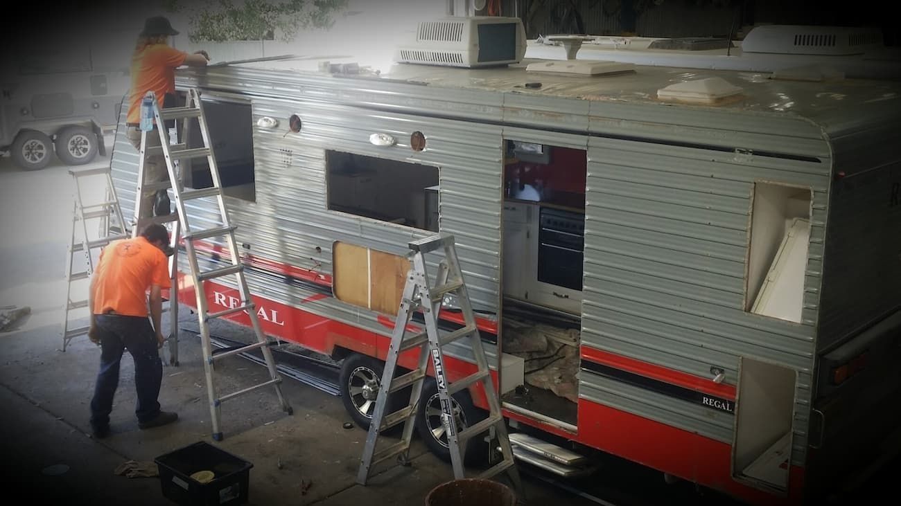 A Man is Standing on a Ladder Next to a Trailer — B & C Caravan Service Pty Ltd In Dubbo, NSW